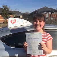 Kerry Frost – Jim #3 200 Kerry Frost smiling and holding her practical first time pass certificate next to the JSF Driving School car.
