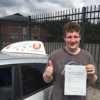 Adam Chandler Driving Test Pass – JSF Jim Adam Chandler giving a thumbs up next to the JSF Driving School car, with a smile, holding his practical driving test pass certificate
