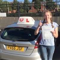 New-Driver-Gloucester-Emily-Barnard-JSF-Driving-School-Instructor-Jim-website A smiling Emily Barnard holding her driving test pass certificate standing next to the JSF Driving School car