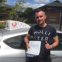 Joe Booth thumbs up with practical driving test pass certificate next to the JSF Driving School car