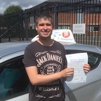 Paul Weyman smiling after his first time practical test pass, holding his certificate by the JSF Driving School car