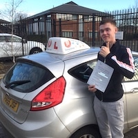 Tom Daykin smiling whilst holding his practical test pass certificate next to the JSF Driving School car