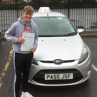 Smiling Dan Afflick after his first time driving test pass next to the JSF Driving School car