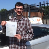 Smiling new driver Liam Bradley holding his pass certificate next to the JSF Driving School car