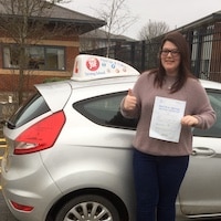 New driver Alex Trigg proudly standing beside the JSF Driving School car holding her first time pass certificate