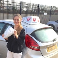 Smiling new JSF Driving School driver Katie Winstone holding her test certificate next to the school car