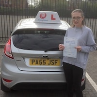 Smiling new JSF Driving School driver Chloe Williams holding her test certificate next to the school car
